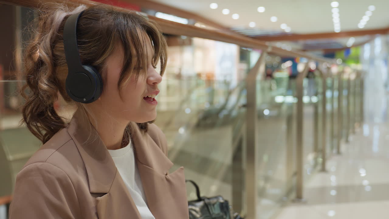 쾌활한 여성 팬이 음악 감상을 통해 행복을 표현하고 있어요. 붐비는 쇼핑몰에서 가장 좋아하는 곡을 부르고 들으면서 행복과 열정을 뿜어내고 있어요.