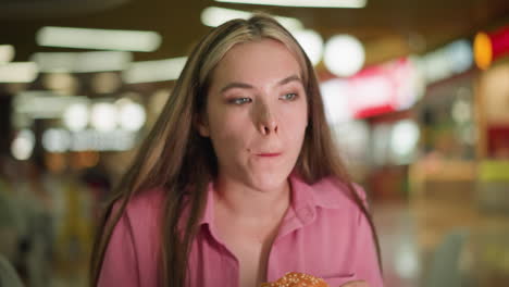 lady in pink dress takes a bite of burger, chewing slowly while contemplating the taste, she appears thoughtful, savoring the food in a relaxed mood, the background has soft bokeh lights