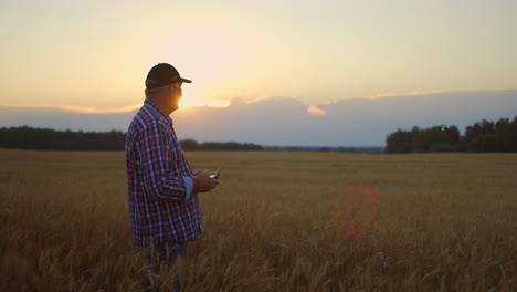 Farmer-holds-remote-controller-with-his-hands-while-quadcopter-is-flying-on-background.-Drone-hovers-behind-the-agronomist-in-wheat-field.-Agricultural-new-technologies-and-innovations.