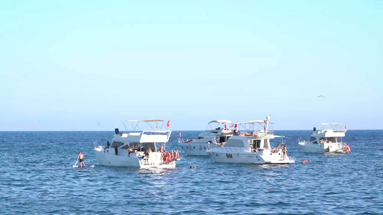 Several yachts anchored in the Mediterranean Sea, with people kayaking and swimming nearby.