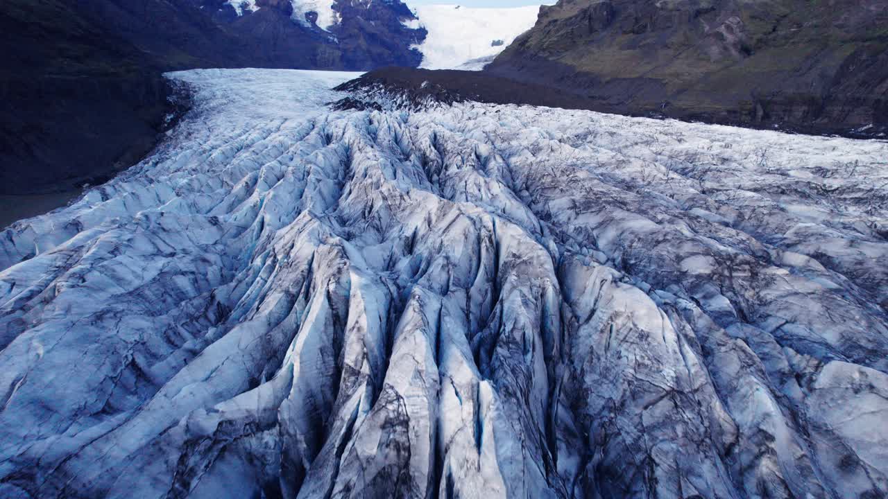 Aerial: A glacier's serpentine path with deep crevasses and jagged ice formations, evidence of the impact climate change has on the constant movement and transformation of this natural wonder