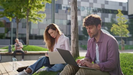 woman making notes outside working laptop. focused adult students study in park