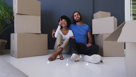 sitting on floor, couple surrounded by moving boxes, smiling and pointing