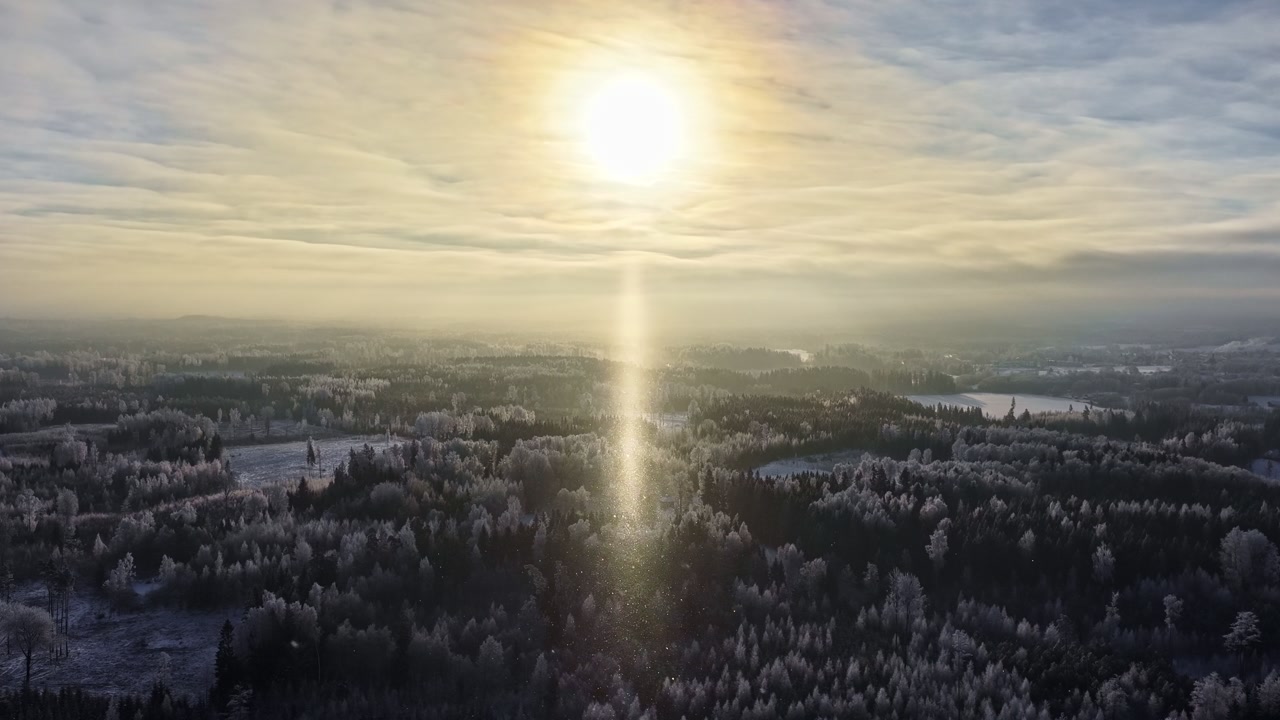 Snow covered rural forest landscape winter season, aerial drone view bright sun behind clouds