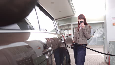 woman filling up car at gas station and drinking coffee
