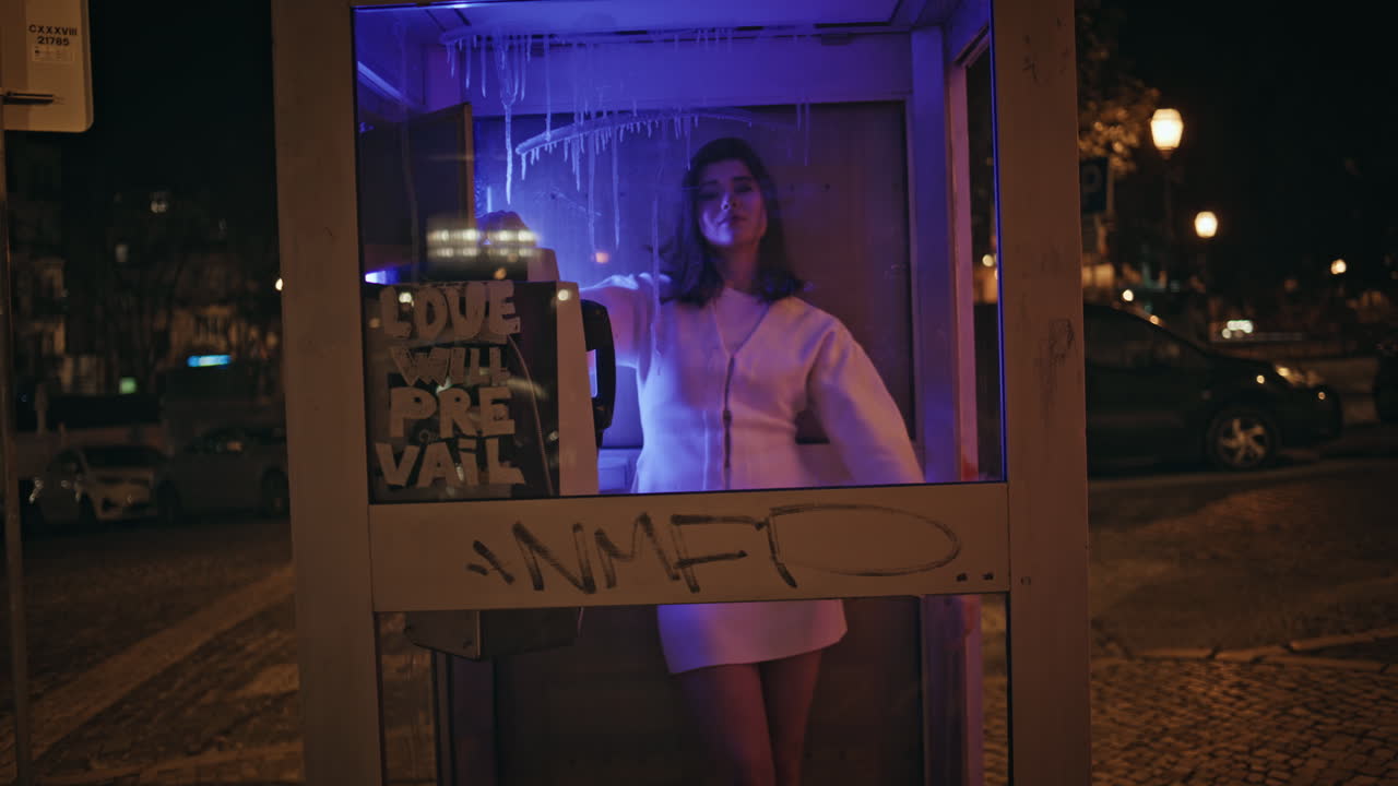 Relaxed girl calling telephone in neon cabin. Fashion model posing at call box