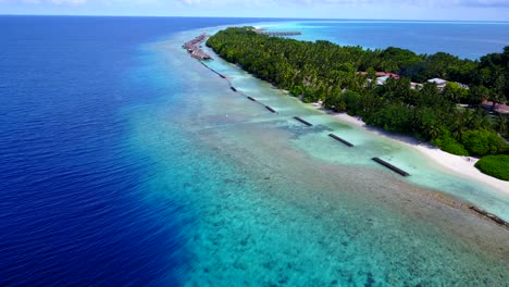 island in maldives - tropical paradise of green trees, white sand, and beach villas surrounded by aqua blue ocean water - aerial shot