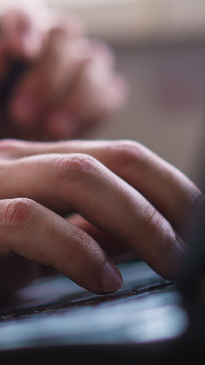 Man with electronic cigarette works on contemporary notebook computer keyboard sitting at table in light office extreme close view slow motion