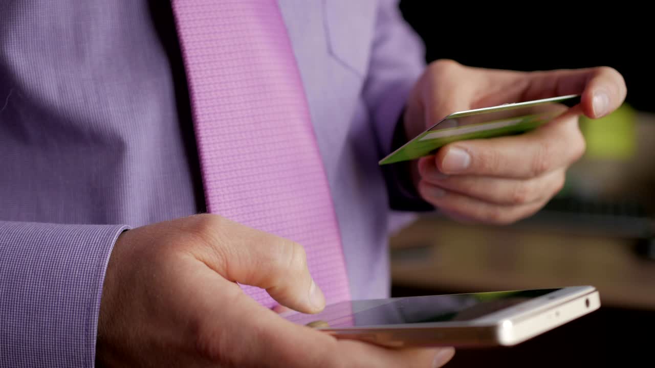 hombre de negocios con una camisa púrpura haciendo pago en línea con tarjeta de crédito y teléfono inteligente, compras en línea, tecnología de estilo de vida. hombre introduce el número de tarjeta bancaria en el teléfono inteligente. primer plano. primer plano