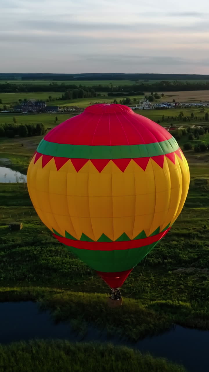 Travel in the air at sunset. Hot air balloon flying in the countryside. Colorful aerostat over the fields and lakes. Aerial view. Motion camera around. Vertical video