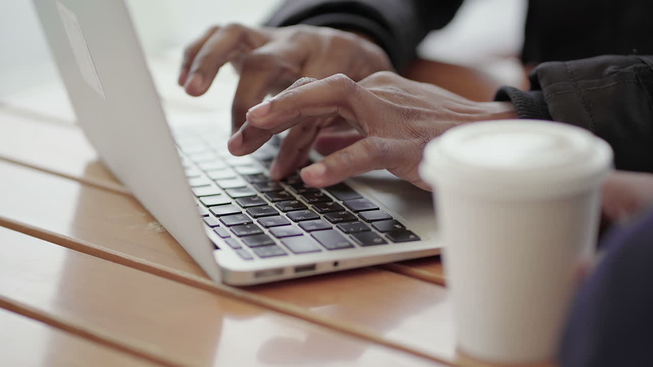 Close up shot of Afro-American middle-aged mans hands typing on laptop