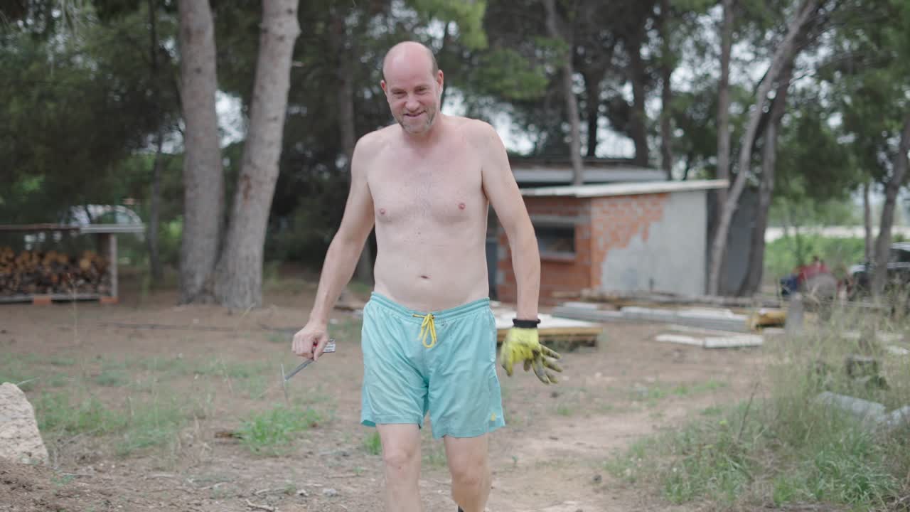 Shirtless Man Walking Outdoors with Fencing Foil and Tools