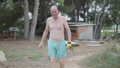 shirtless man walking outdoors with fencing foil and tools