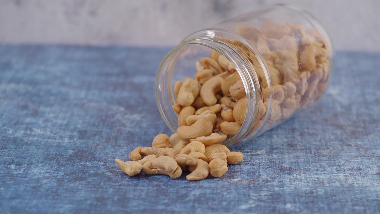 Cashewnøtter som velter ut av et glass på en blå overflate