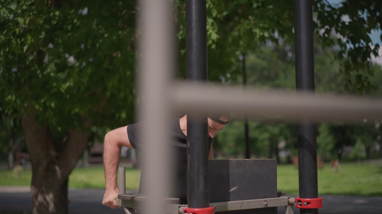 White Man Straining On Dip Bars With Visible Effort And Tight Form, Close Framing On Hands And Face, Leafy Park Background And Concentrated Expression, Athletic Intensity And Focus