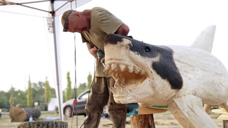 woodcarver working on a large wooden shark sculpture