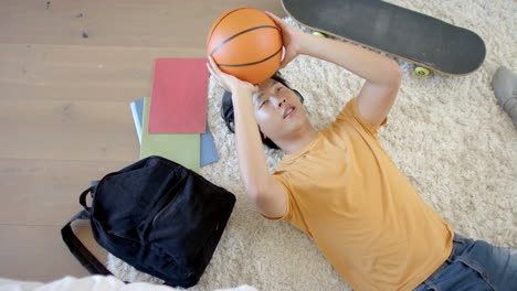 teenage asian boy lies on a carpet at home throwing a basketball