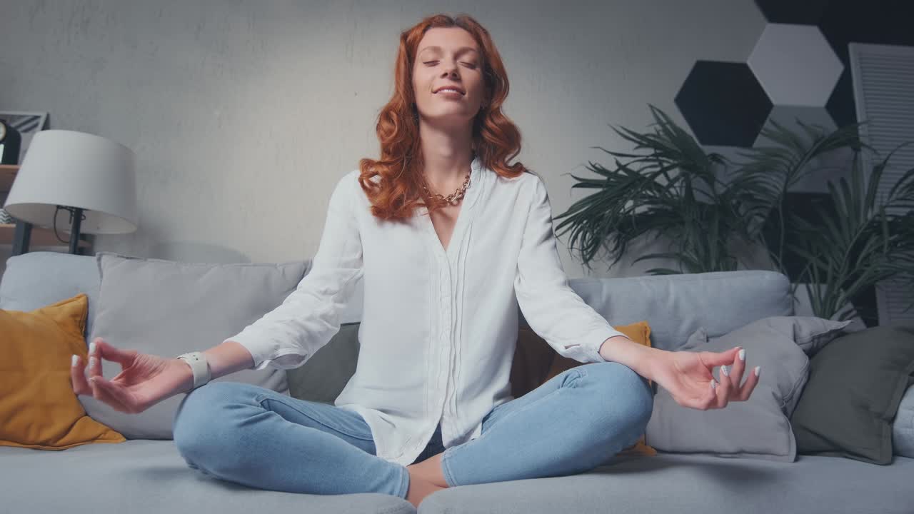 Woman sit cross legged on sofa in living room closed eyes do meditation practice