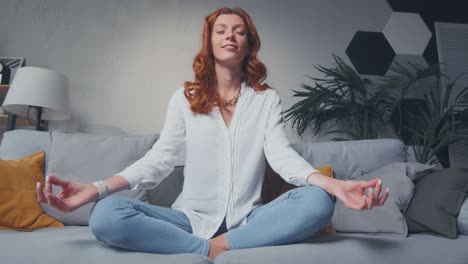 woman sit cross legged on sofa in living room closed eyes do meditation practice