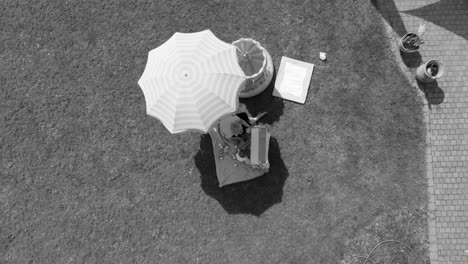 slowly ascending above a mother and child sitting in the shade of an umbrella, aerial black and white