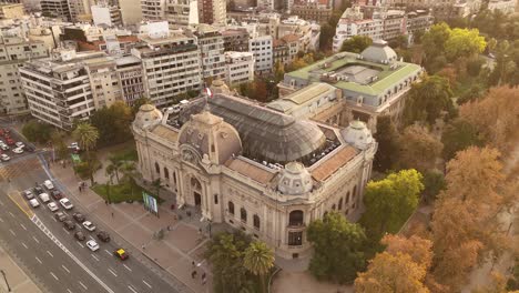 fine art national museum with waving flag of chile at sunset time. de chile with housing area apartment block an d colored trees. traffic on street. aeral orbit wide shot.
