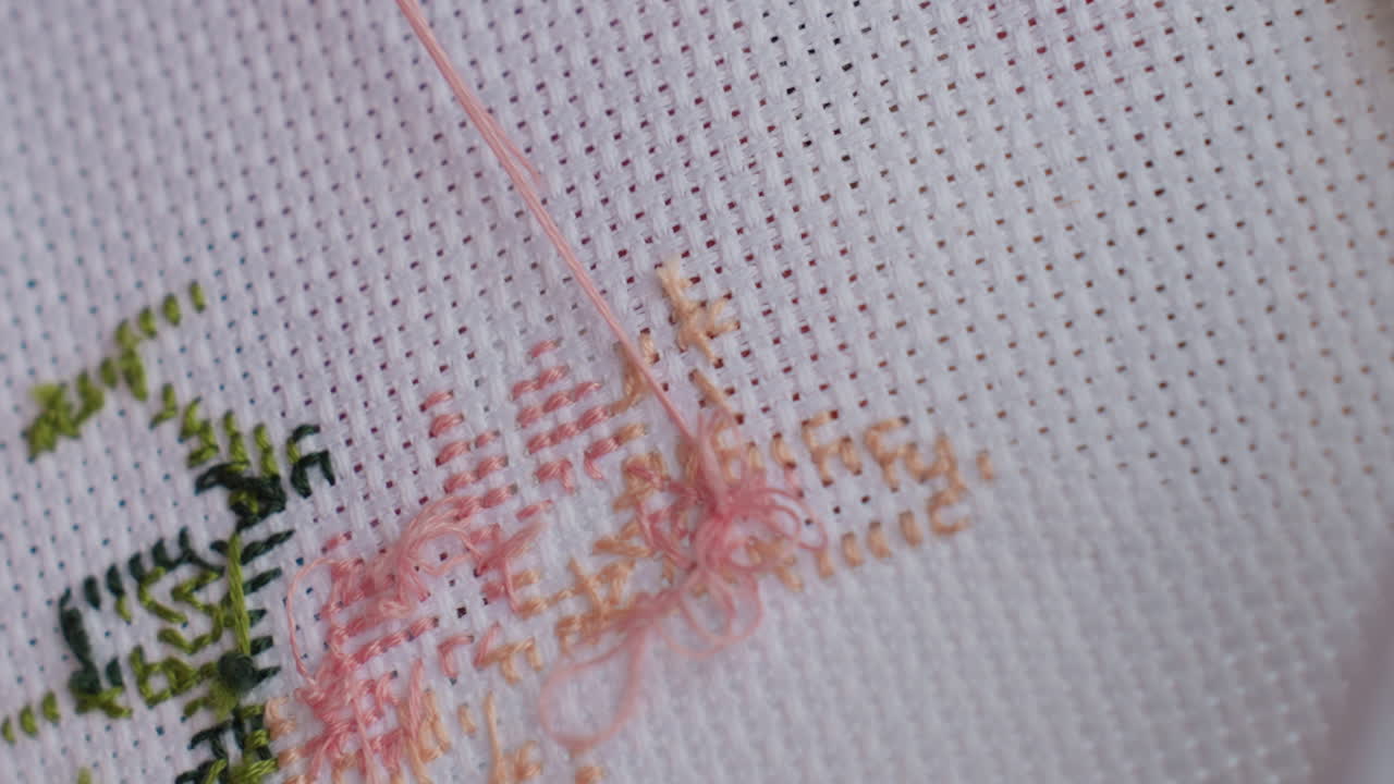 Extreme close up craft person embroidering fabric using fine hand motion, soft focus showing calm concentration, gentle touch guiding needle through cloth texture