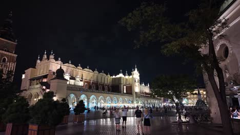 Nighttime view of the historic Church of St. Wojciec with a green dome in Krakow's Main Square, framed by trees
