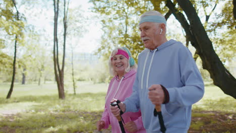 Cheerful-senior-old-couple-grandfather,-grandmother-training-Nordic-walking,-running-in-summer-park