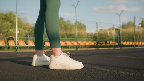 side view of woman legs in green leggings bouncing volleyball outdoors with seating area and trees in background, showcasing active lifestyle and athletic energy in vibrant urban setting