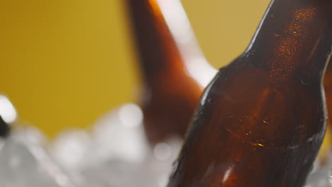 cerrar las botellas de vidrio de cerveza fría o refrescos que se enfrían en un cubo lleno de hielo contra un fondo amarillo 2