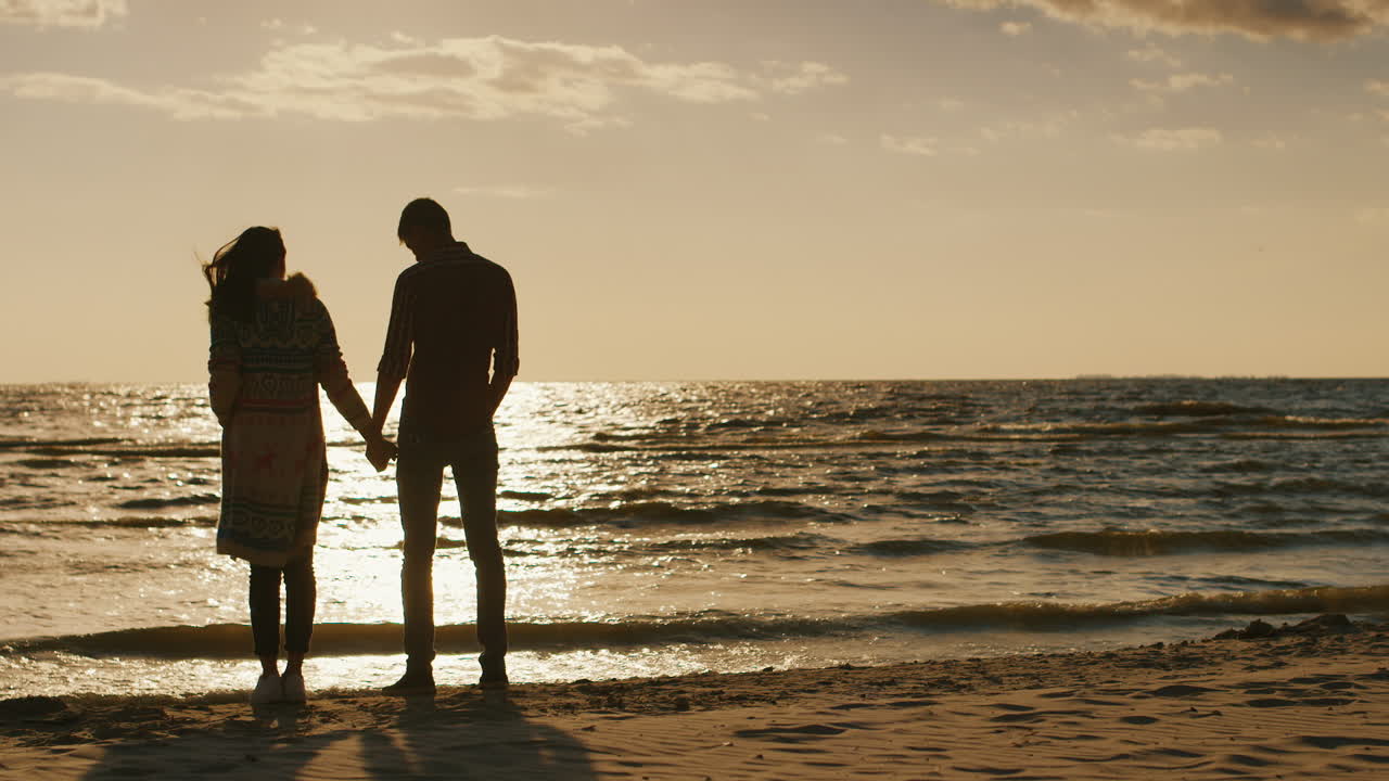 바람이 부는 시원한 날을 품은 바다의 일몰을 감상하는 젊은 부부의 실루엣