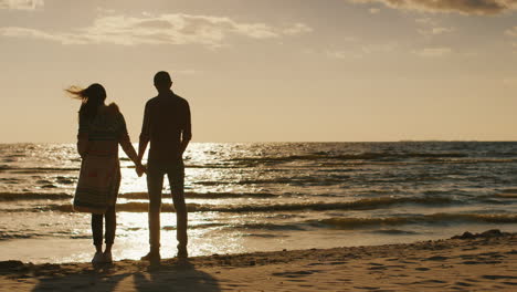 silhouettes of young couple admiring the sunset on the sea embracing cool day the wind blows