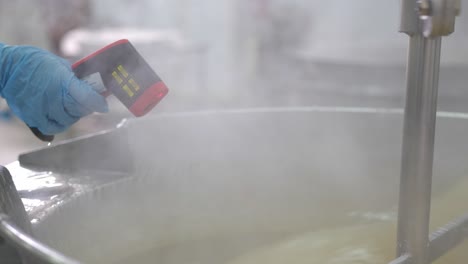 usando una pistola de termómetro infrarrojo para verificar la temperatura en un lote de delicias turcas en una tina en la fábrica