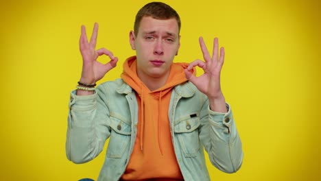 young man in casual wear smiling and making okay gesture with his hand.