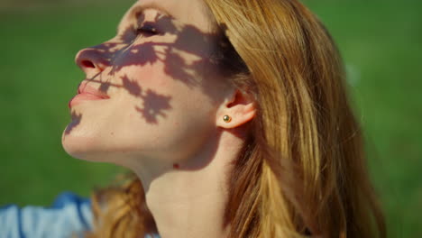 closeup pretty girl face enjoying sunshine in park. branch shadow on woman face.