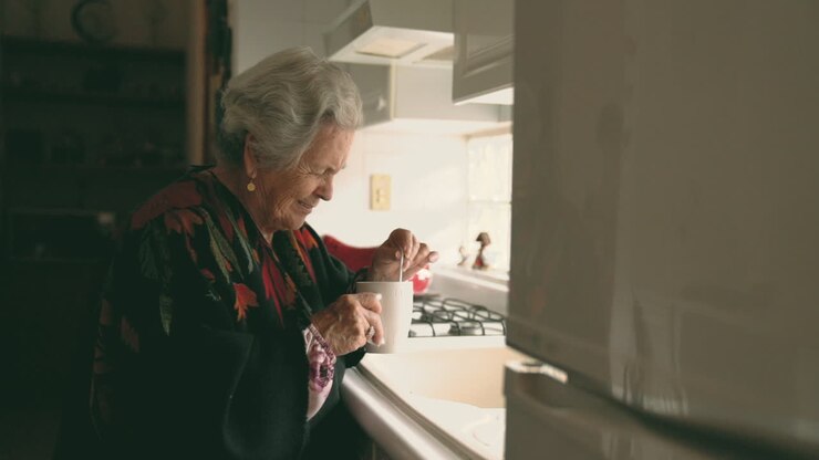 Smiling senior woman in warm clothes with mug near sink