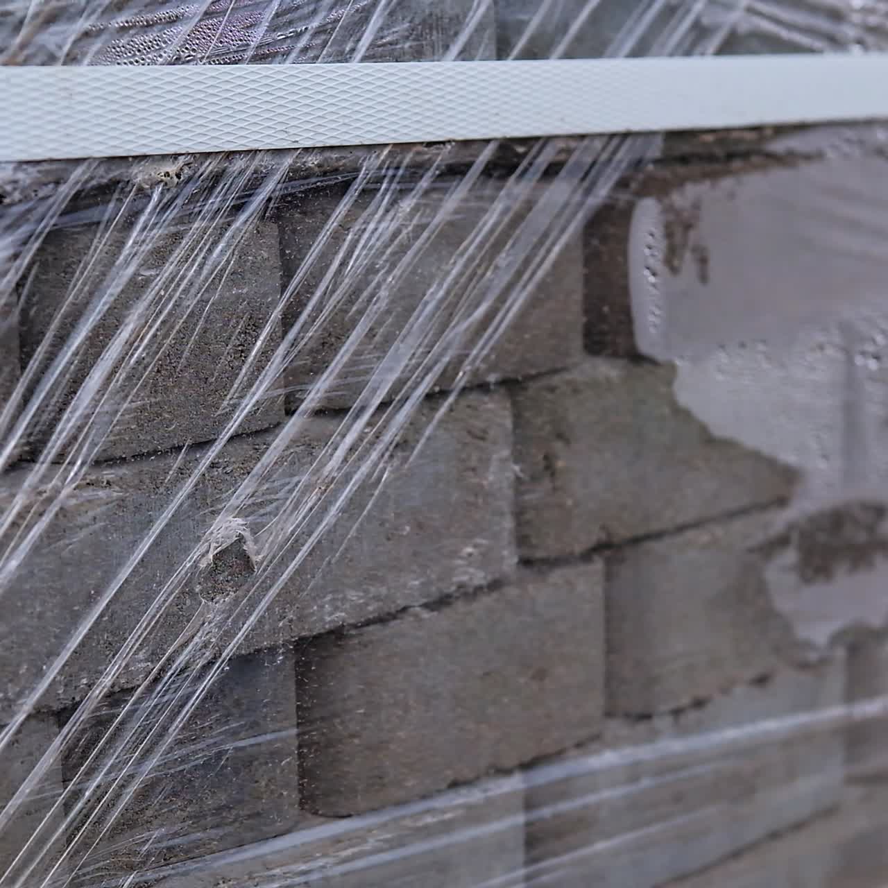 Sidewalk grey bricks in a big pile covered with cellophane. Close up. Plastic band holding stack together