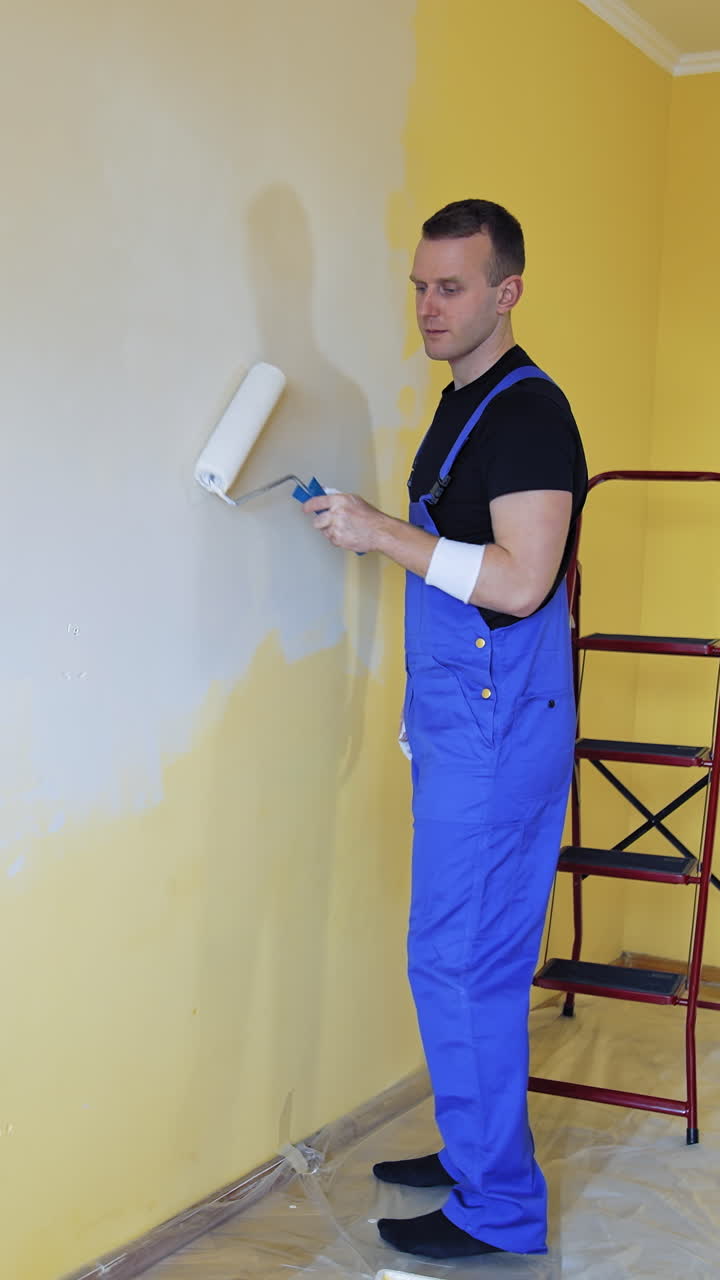 Handsome man with painting roller doing new indoor improvement. Professional builder renovating house. Vertical video