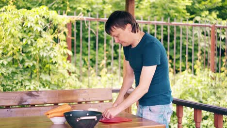 young guy is cooking pilaf he is in a summer house cuts meat on a red cutting board