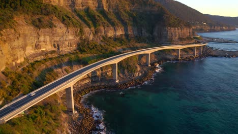 car travelling at sea cliff bridge over blue sea in sunrise at sydney, nsw, australia