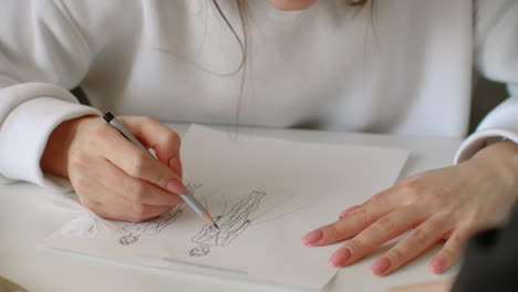 close up of two young women working as fashion designers and drawing sketches for clothes in atelier