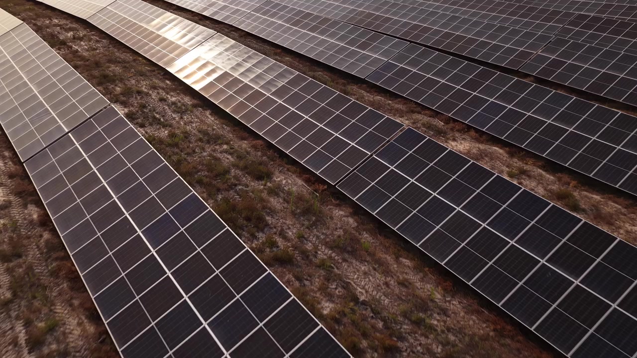 Luftoptagelser af store solcelleanlæg på en solbeskinnet italiensk solcellepark om sommeren, der fremhæver bæredygtig energi, geometriske mønstre og et naturligt landskab med tørt græs.