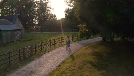 drone aerial shot of woman riding bike along country lane at sunset