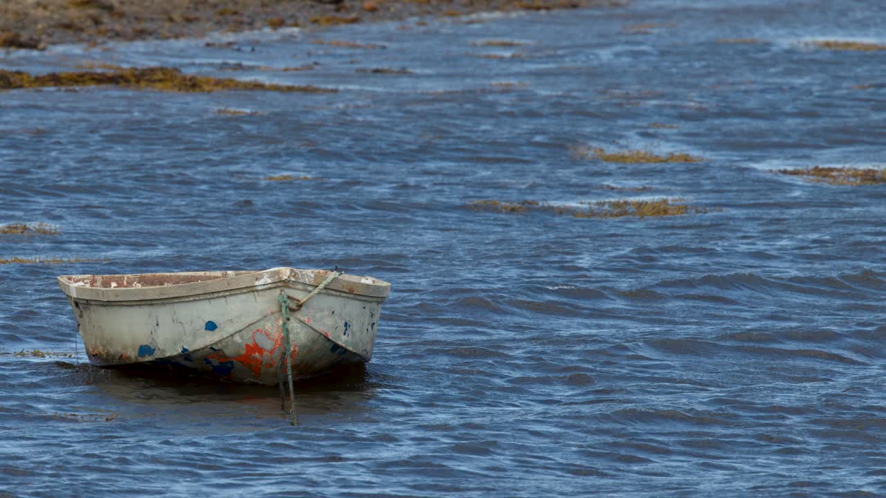 Weathered rowboat gently rocks on blue water near shore, captured with steady camera, natural light