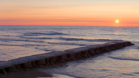 Serene sunrise over Lake Michigan with gentle waves rolling toward camera, a pier in the foreground, and a lone surfer in the distance as the camera drifts smoothly