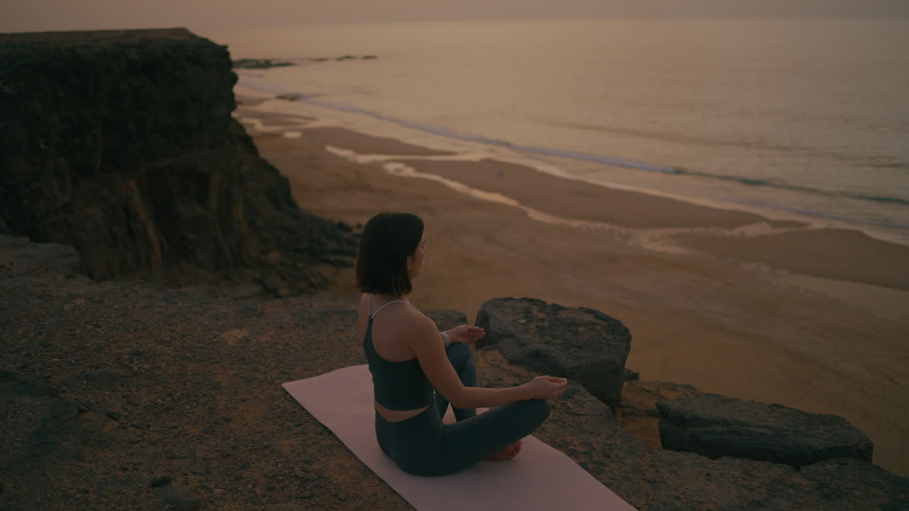 Woman Meditating on a Cliff Above the Beach at Sunset