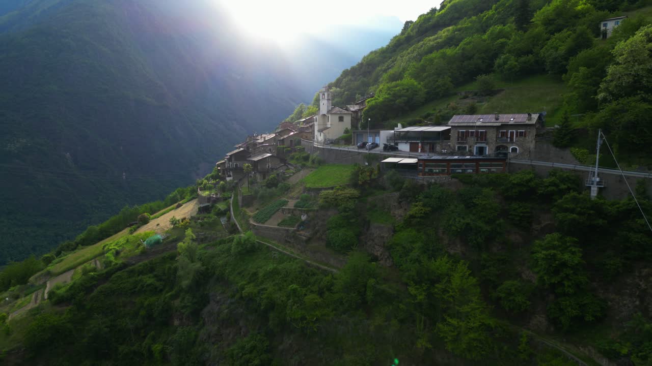Sunlight breaks over a remote Italian mountain village clinging to a steep hillside, casting dramatic shadows. Shot at Tirano, Italy