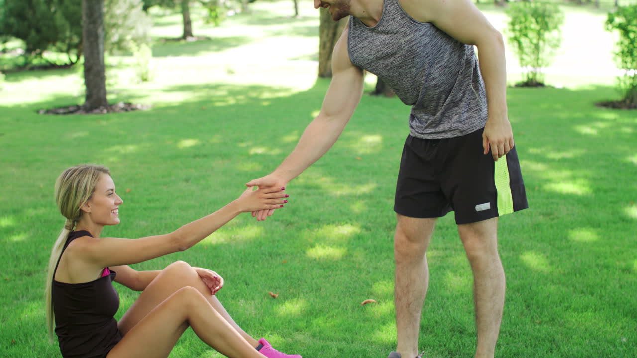 el atleta ayuda a la joven a levantarse del césped verde. personas deportivas trabajo en equipo