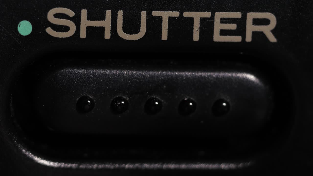 Macro close up of finger pressing shutter button with teal dot and grey lettering