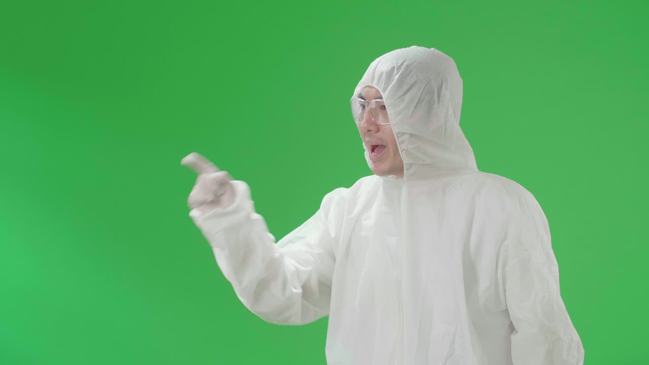 Side View Of Angry Asian Man Wearing Personal Protective Equipment Uniform Ppe And Pointing Displeased And Frustrated In The Green Screen Studio